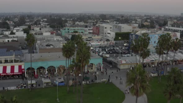 AERIAL: Over Venice Beach Boardwalk with Visitors and Palm Trees, Sunset, Los Angeles, California 