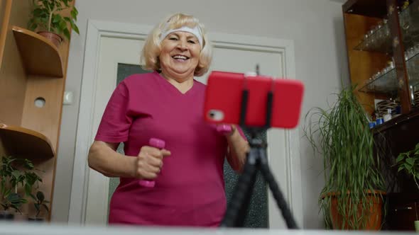 Senior Elderly Old Woman Watching Online Distance Workout Exercises with Dumbbells on Mobile Phone