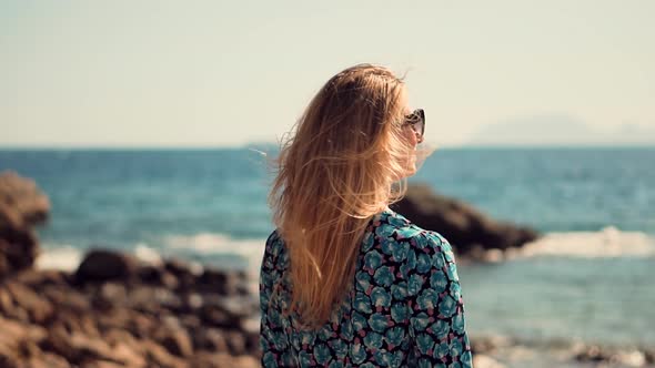 Woman Tourist Stands On Shore Enjoying Marine Views. Rocky Seacoast Beach. Girl Looking At Ocean.