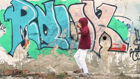 The boy is dancing in front of the graffiti painted wall. alt