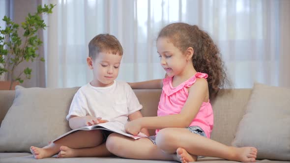 Cute Children,sister with a Younger Brother, Looking at a Book Magazine Textbook Dictionary Tablet