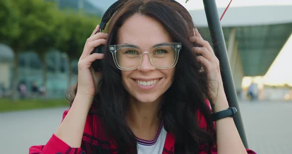 Brunette in Stylish Glasses which Putting on Headphones and Looking Into Camera