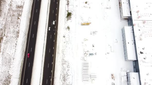 Commercial building construction site covered in white snow near highway road with many cars, aerial