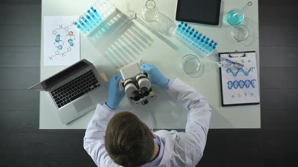 Top View of Lab Worker Putting Prepared Sample on Stage to View Under Microscope