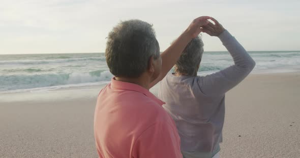 Happy hispanic senior couple dancing on beach at sunset
