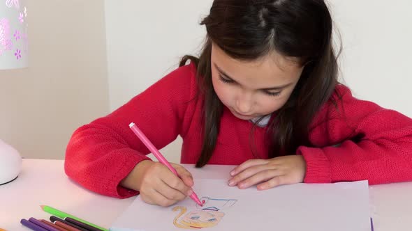 A young girl coloring a drawing with a vibrant pink marker at a small table.