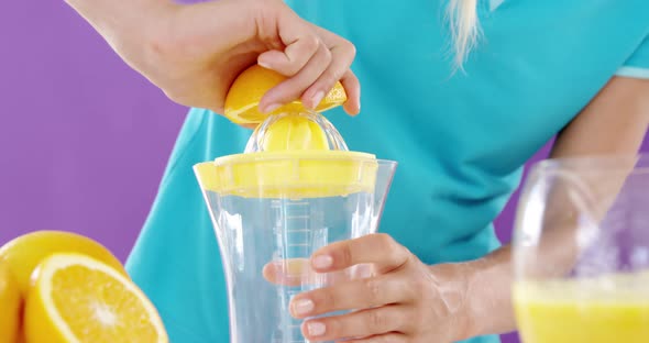 Woman preparing sweet lime juice from juicer against violet background