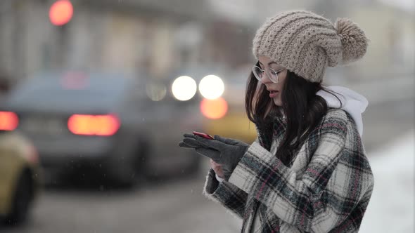 Young Woman Is Recording Voice Message on Smartphone Standing Outdoors in Big City at Winter Day