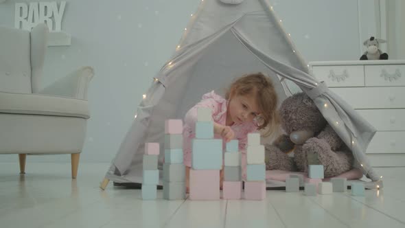 Little Girl in Pink Pajama Playing with Wooden Blocks Sitting in Kids Tent with Bear and Bunny