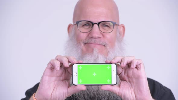 Face of Happy Mature Bald Bearded Man Thinking While Showing Phone
