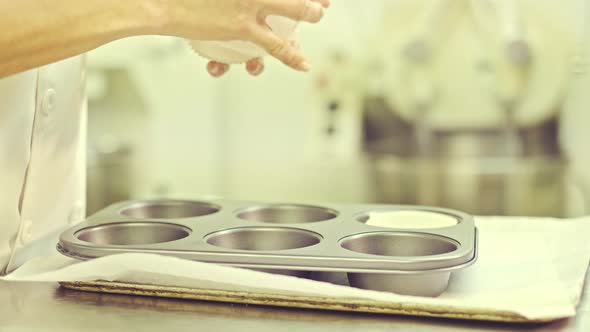 Confectioner putting paper cups into baking forms for muffins