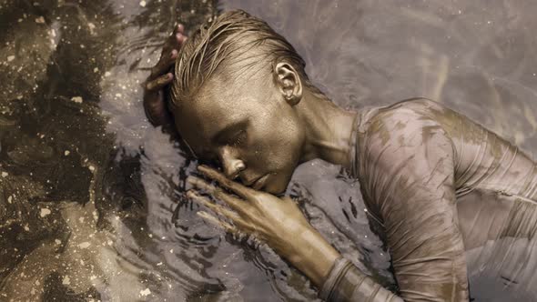 Unusual Fashion Shot with Tender Woman Covered Golden Paint in Water Moving Slowly