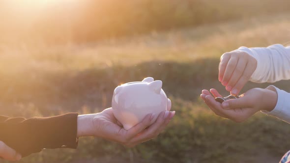 Hands Mother and Daughter Child Putting Coins Into Piggy Bank. Woman Holds Piggy Bank While Girl