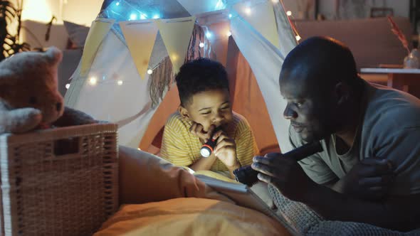 Cheerful Afro-American Dad Reading Book to Son before Bed