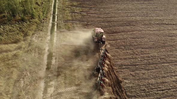 Powerful Tractor with a Plow Cultivating the Field and Raising Huge Clouds of Brown Suffocating Dust