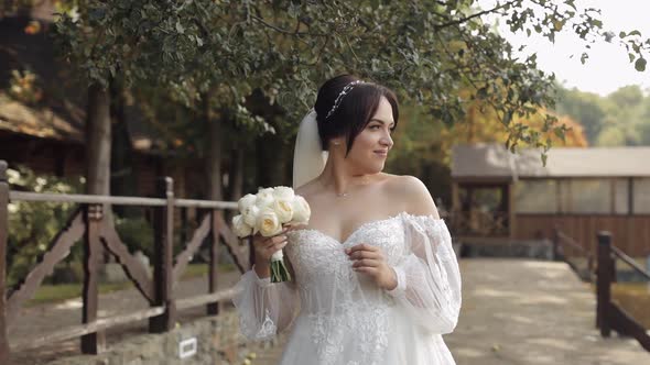 Beautiful Stylish Bride in White Wedding Dress and Veil Holding Wedding Bouquet in Hands in Park