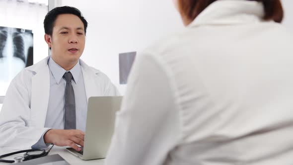 Asia male doctor great news talk symptoms with female patient sitting at desk in health clinic