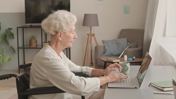 Senior Woman in Wheelchair Typing on Laptop at Home