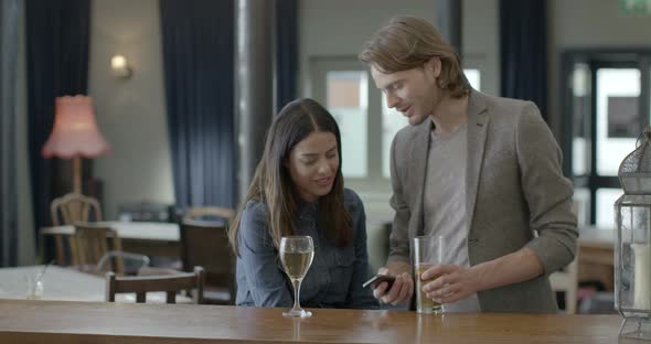 Man holding mobile phone and talking with woman in pub