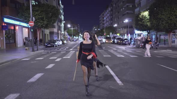 Beautiful Women In Witch Costume Laughing And Playing With Witch's Brooms In The Street