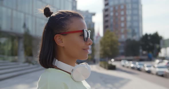 Close Up of Mixedrace Woman in Sunglasses with Headphones on Neck Standing Outdoors