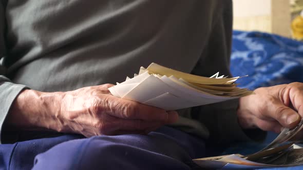 Close-up of the hand of an elderly man holding a pile of old black and white photographs from the fa