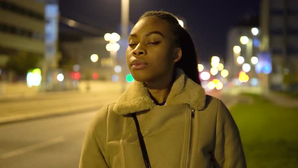 A Young Black Woman Looks Around in a Street in an Urban Area at Night