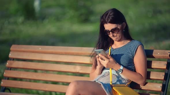 Beautiful Woman Sitting on the Outdoor Bench and Typing on the Phone