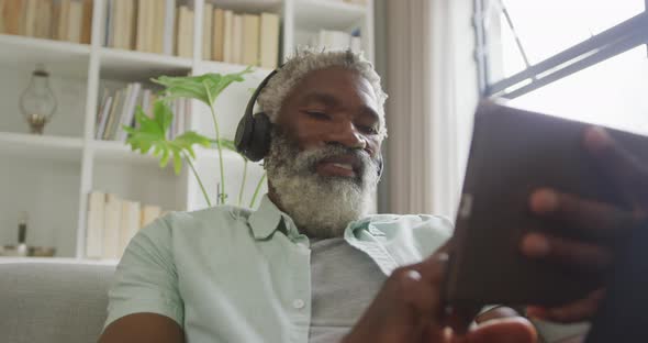 Video of african american senior man using tablet and headphones