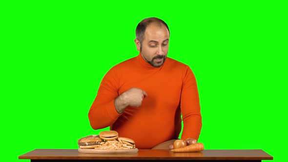 Full Caucasian Male at the Table Chooses Between a Plate of Fast Food and Healthy Food, Stops at