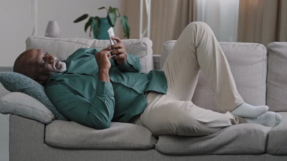 Elderly African American Man Lying Lazily on Cozy Couch in Apartment Pensioner Killing Time Chatting