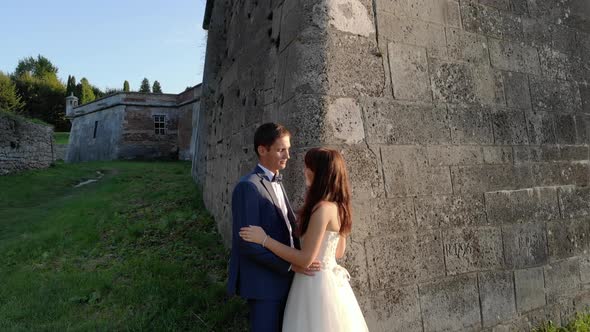 Happy Newlyweds at Sunset, Standing at the Castle Wall. The Sun Is Shining Into the Camera