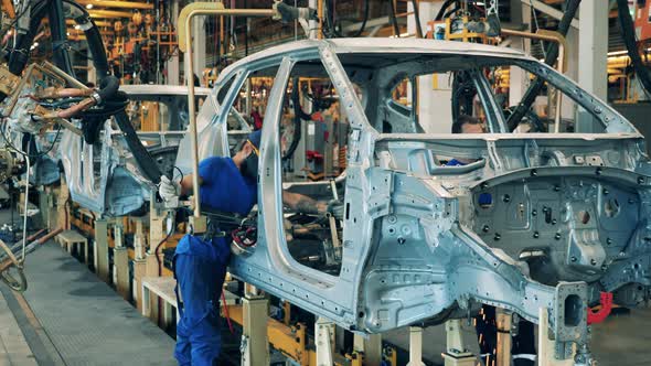 Several Car Factory Workers Using a Welding Machine on a Car Assembly Line