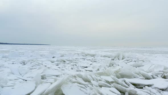 Slowly flying over frozen lake at blue hour. Drone footage of ice covered water on a overcast day.