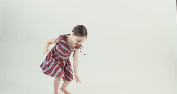 Little girl wearing a dress dances on a white studio background