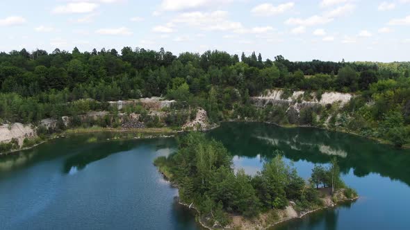 Aerial View of lake with a Small Island and Beautiful Water in a Quarry Surrounded by Forest Trackin