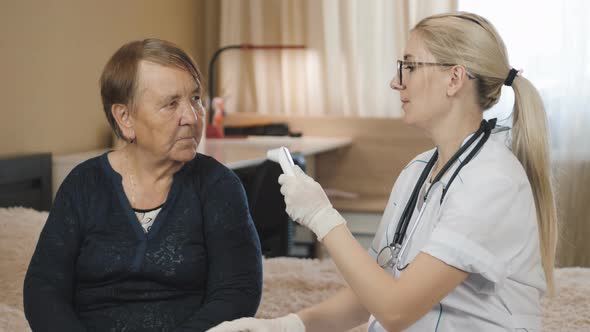 Old woman and doctor. Home visit. Medical consultation grandma at home. Measures the temperature.