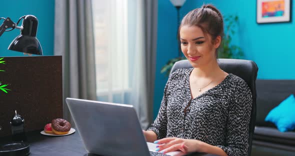 A Young Pretty Brunette Girl Uses a Laptop While Sitting at a Desk in a alt