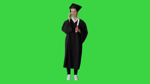 Emotional Female Student in Graduation Robe Talking on the Phone Holding Diploma on a Green Screen