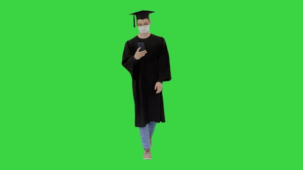 Young Man with Graduation Gown Walking in Medical Mask Using Smartphone on a Green Screen, Chroma