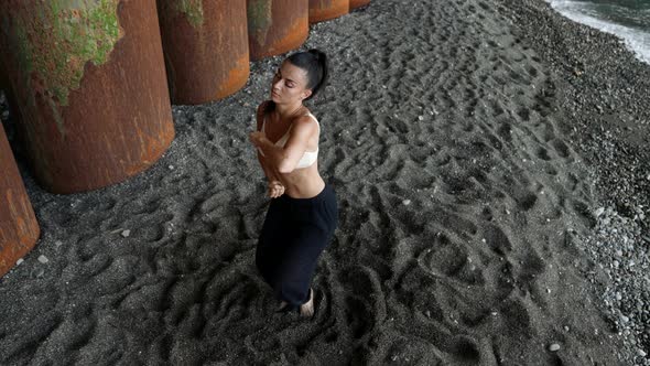 a Barefoot Woman Dances By Rusty Large Columns on Black Sand