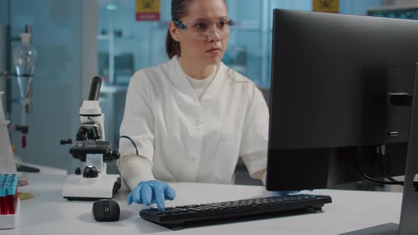 Specialist with Safety Goggles Using Microscope in Laboratory