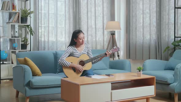 Asian Woman Composer With Paper And Smartphone Playing Guitar At Home