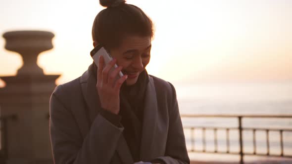 Caucasian Woman Speaking Mobile Phone and Laughing During Sunrise at Sea in Slowmotion