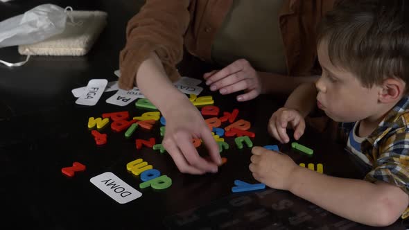 Mom teaches her son how to say the words on the cards and letters at home at the table