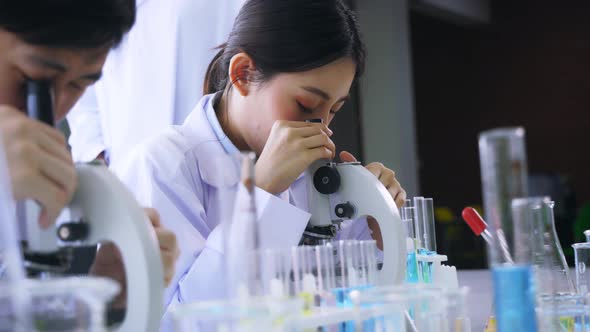 Young Asian Female Scientist Doing Research in Laboratory Wearing Lab Coat and Gloves with Colleague