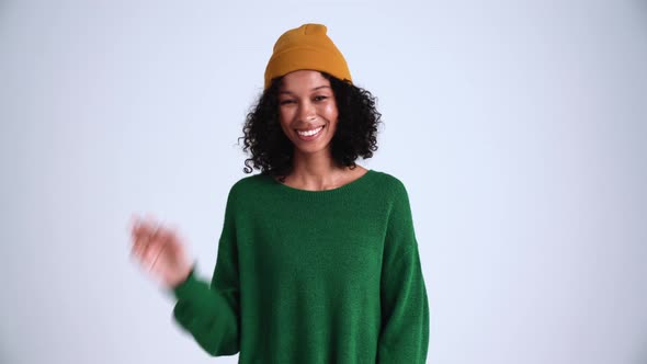 Smiling curly-haired woman wearing hat showing hello gesture