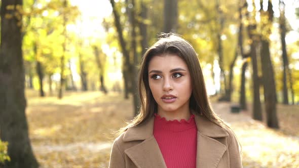 Portrait of Brunette Admires the Nature of Autumn Park with Light Smile