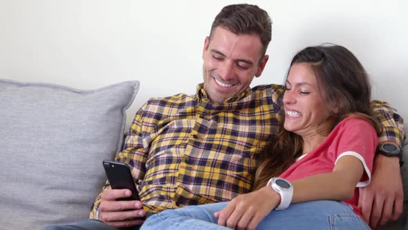 Cute couple using mobile phone in living room at home 4k