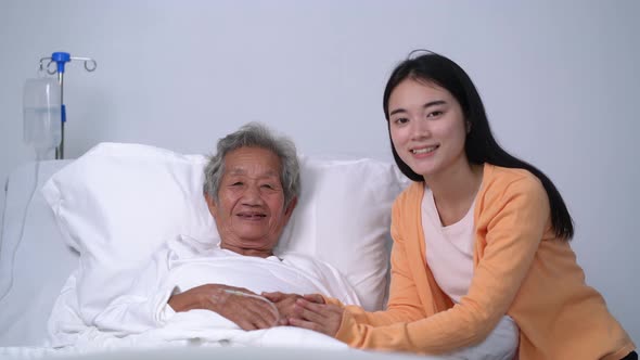 Old patient and daughter smiling at camera in hospital bed